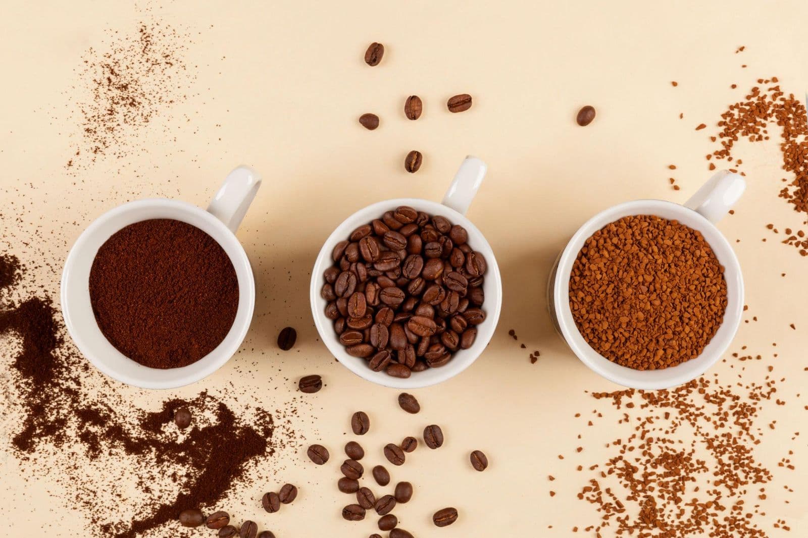 Ground coffee, roasted coffee beans and instant coffee granules in three cups
