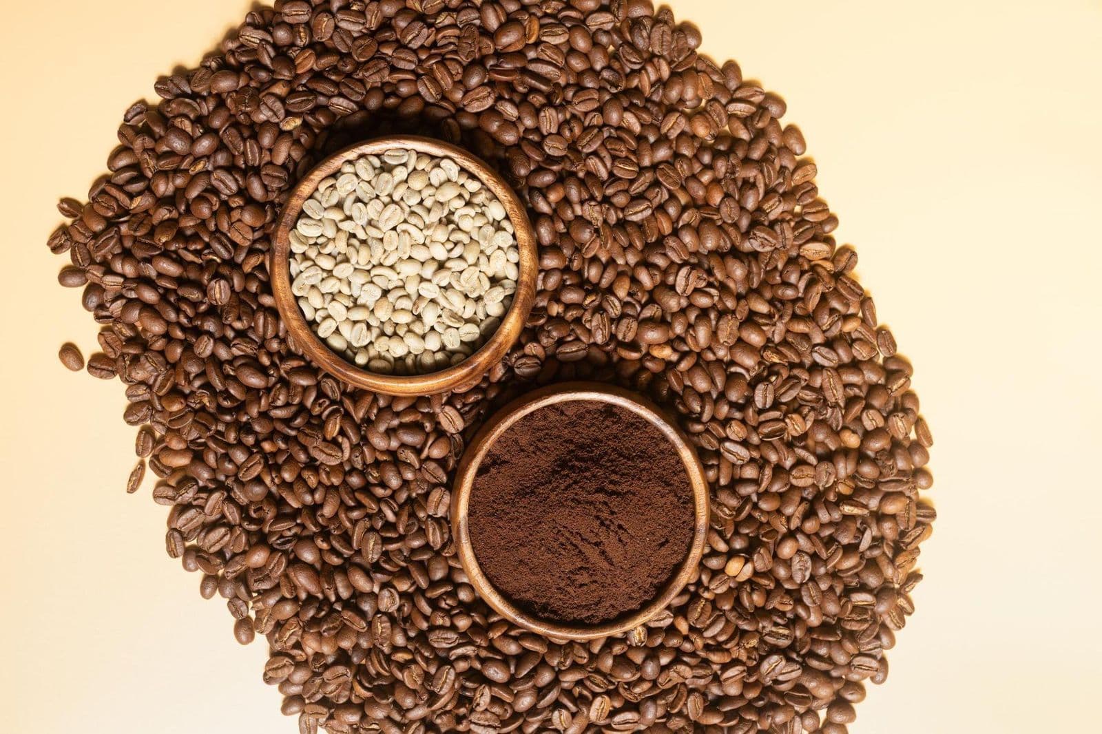 Green coffee beans and ground coffee in wooden bowls on roasted beans
