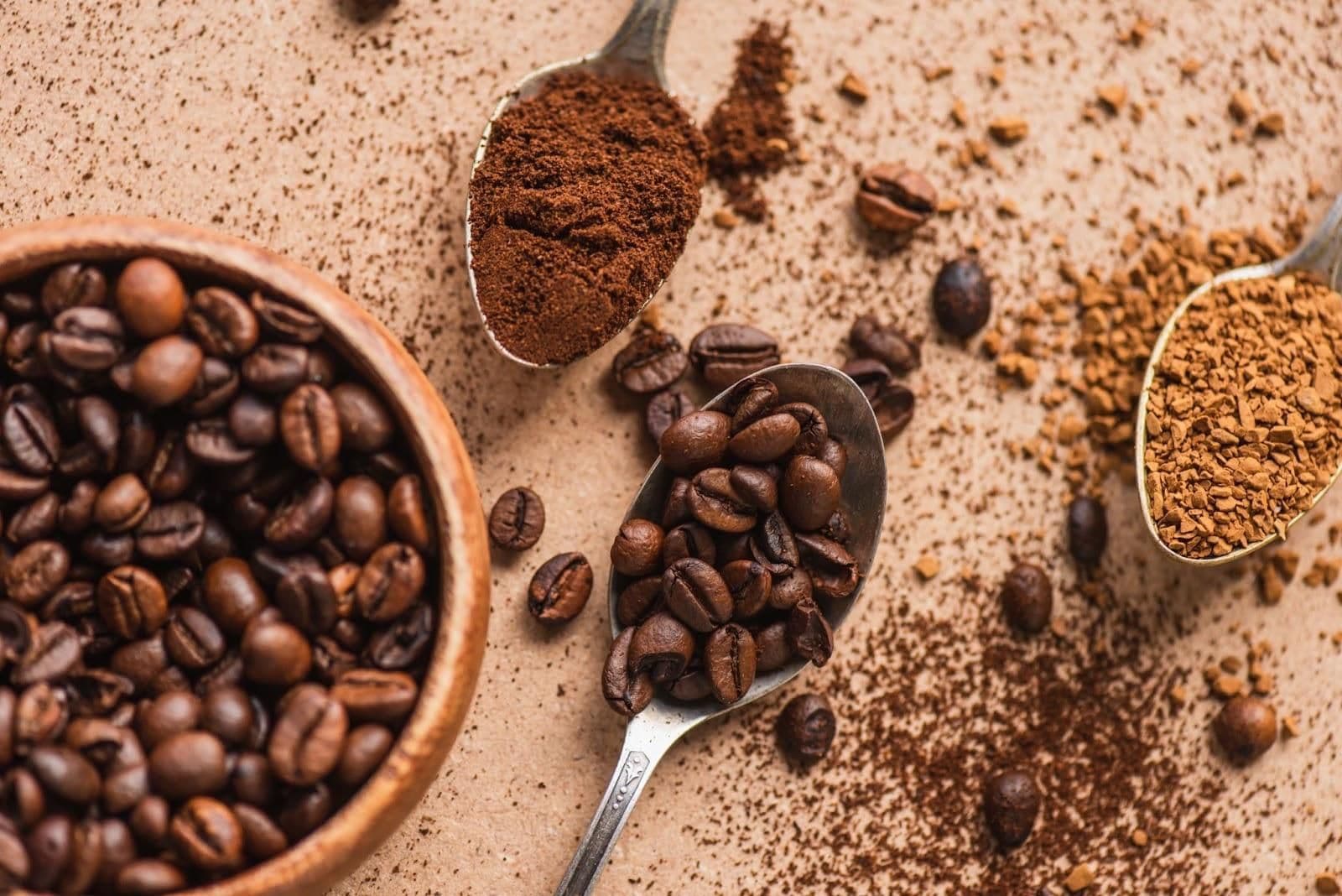 Roasted coffee beans in a wooden bowl with spoons of ground and instant coffee