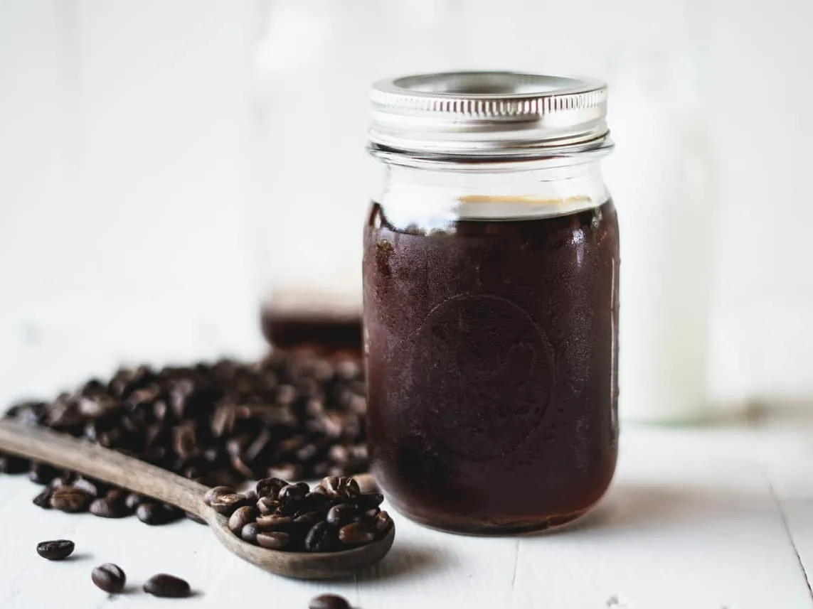 Dark coffee concentrate in a glass jar beside roasted beans