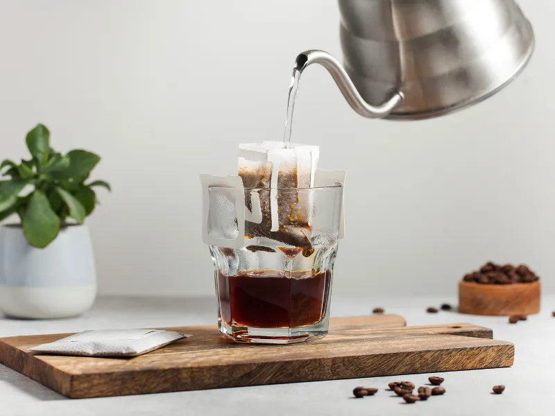 A drip coffee bag brewing in a glass as hot water is poured