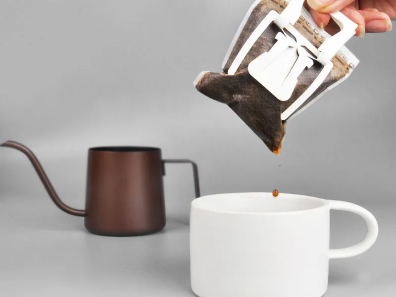 A used drip coffee bag lifted from a white cup