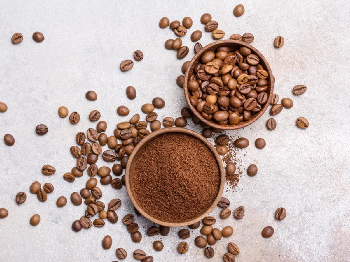 Roasted coffee beans and ground coffee in two wooden bowls