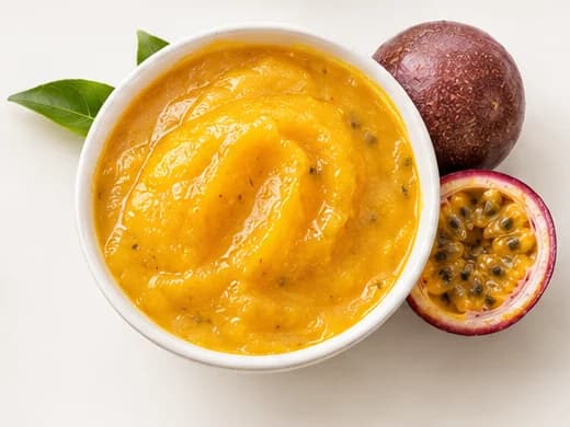 Passion fruit purée in a bowl with whole and halved passion fruit