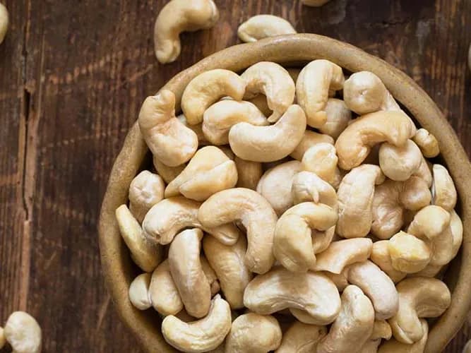 Cashew kernels in a wooden bowl on a dark table